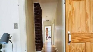Un pasillo con suelo de madera, una pared de ladrillo decorativa y una puerta de madera.
