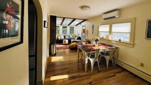 Un comedor con suelo de madera, una mesa con sillas y vistas a una sala de estar con sofá y cojines.