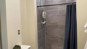 A shower area with a dark curtain, tiled walls, and a white bathtub.