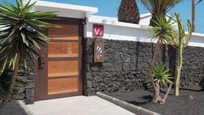 A modern building with a wooden door, a stone wall, and tropical plants.