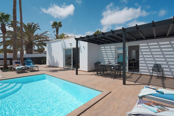 A pool area with a clear blue pool, lounge chairs, and a pergola. - Casa Afortunada, the pleasure of relaxation (Costa Teguise)