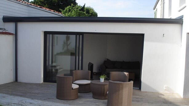 Un patio con mobiliario de mimbre, una puerta corredera de vidrio y una planta pequeña.