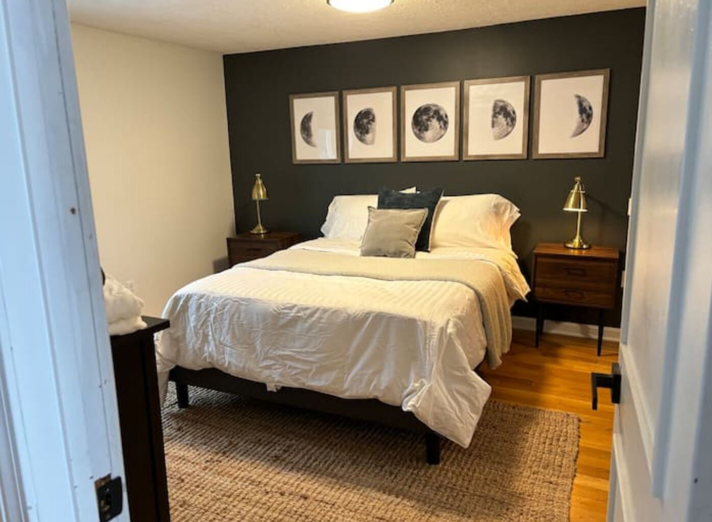 Une chambre à coucher comprenant un lit, deux tables de chevet, un tapis et des œuvres d’art murales représentant des lunes.