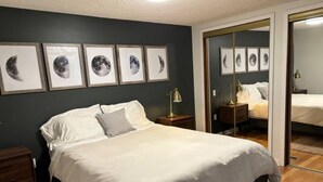 Une chambre à coucher avec un lit, une table de chevet, une lampe et un mur orné de reproductions des différentes phases de la lune.