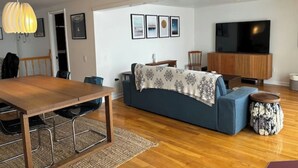 Un salon moderne avec une table à manger en bois, un canapé bleu et un téléviseur posé sur un meuble en bois.