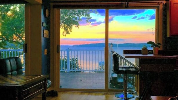 Une pièce dotée d’une grande porte-fenêtre coulissante donnant sur un balcon avec vue sur le coucher de soleil sur l’eau.