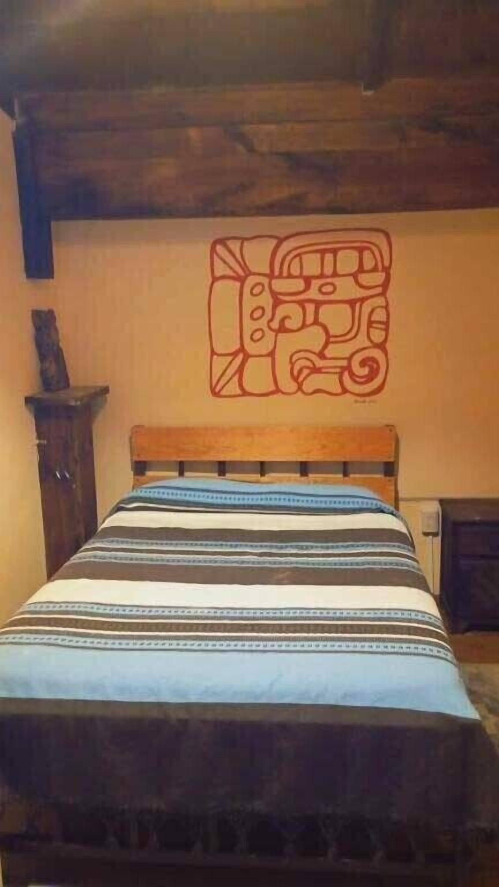 A bed with a striped bedspread, a wooden headboard, and a wall with a red geometric design.