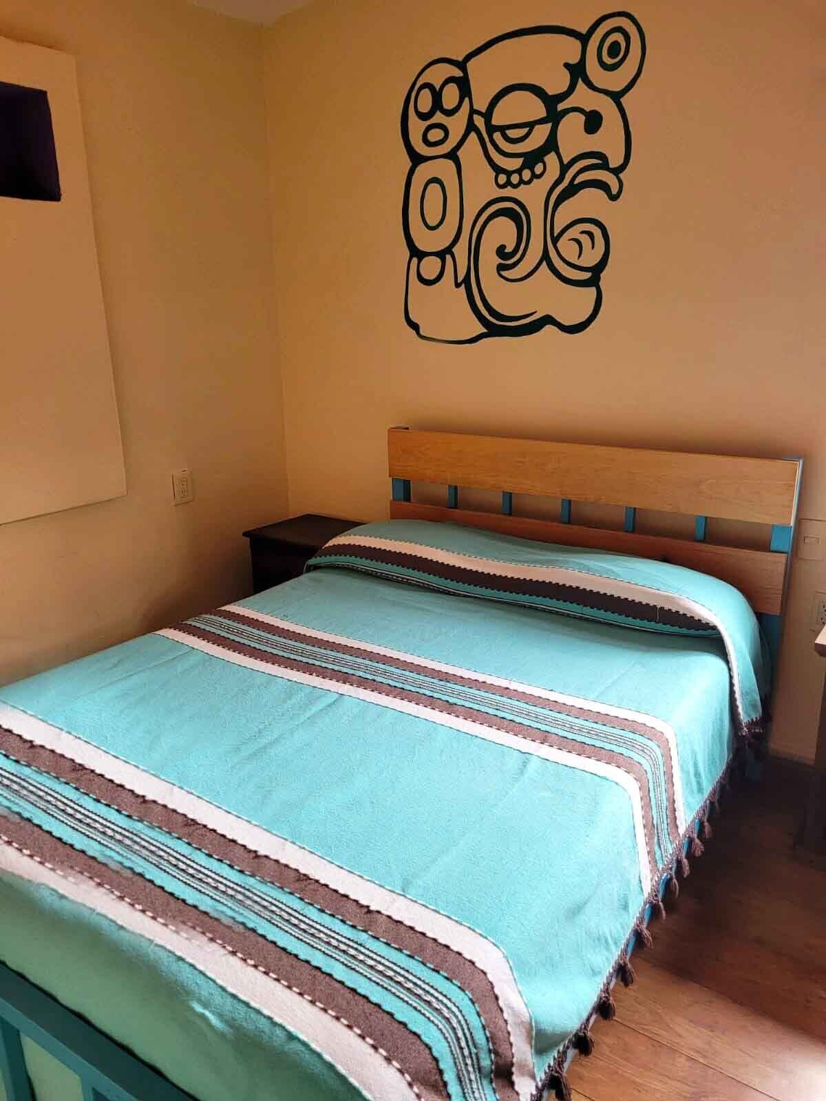 A bedroom with a bed, a wooden headboard, a wall decal, and a nightstand.