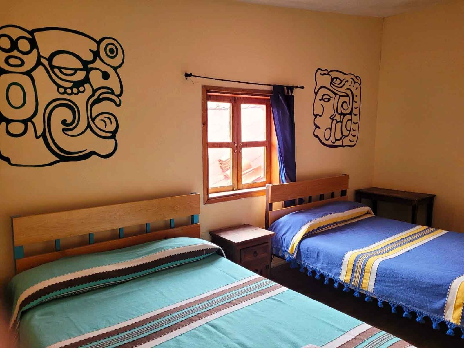 Ein Zimmer mit zwei Holzbetten, einem Vorhangfenster und Wandbildern.
