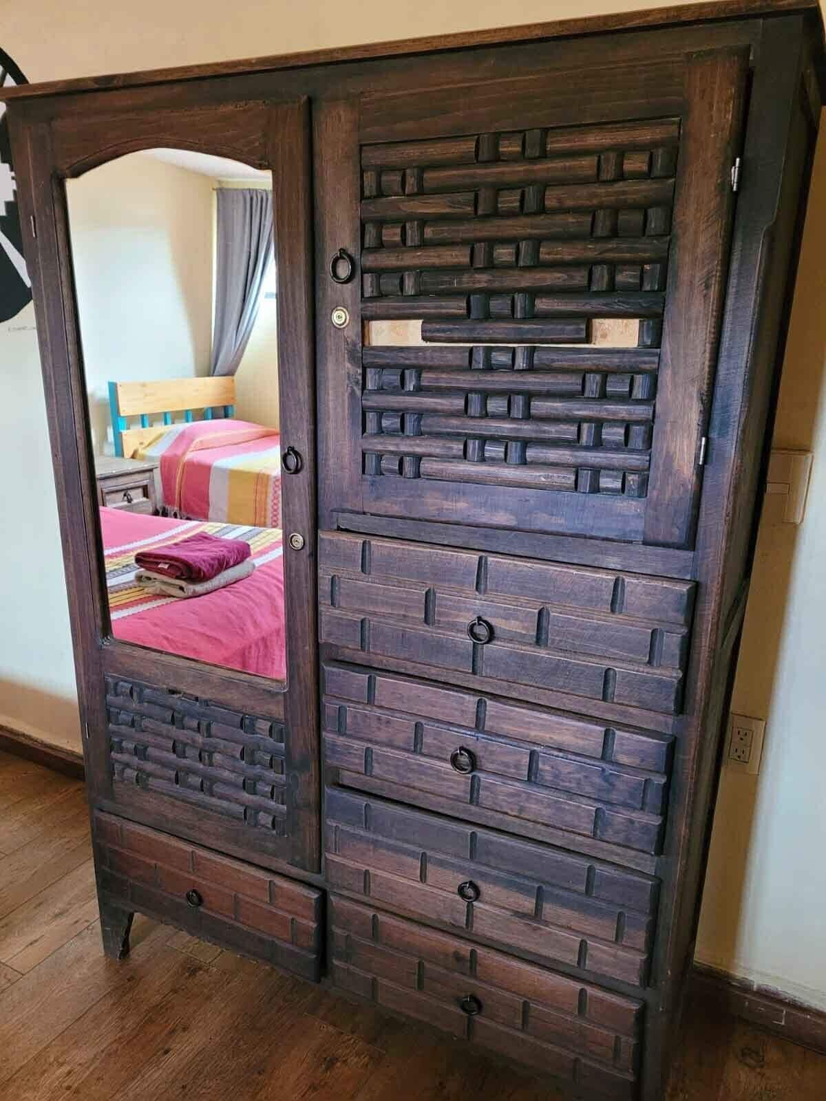 A wooden wardrobe with multiple drawers and a mirror.