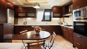Une cuisine moderne avec des meubles de couleur bois foncé, des appareils électroménagers en acier inoxydable et une table de salle à manger ronde, assortie de chaises.