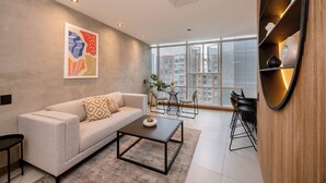 A modern living room with a sofa, coffee table, and a large window offering a city view. - Premium 1BR Apt with Jacuzzi & A/C in El Poblado (Medellín)