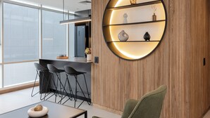 A modern interior with a wooden panel wall, a circular shelf with decorative items, a bar area with stools, and a large window providing natural light. - Premium 1BR Apt with Jacuzzi & A/C in El Poblado (Medellín)