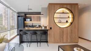 A modern kitchen with a central island, bar stools, and a wooden accent wall with a circular shelf. - Premium 1BR Apt with Jacuzzi & A/C in El Poblado (Medellín)