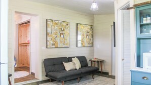 Tunnelmallinen olohuone, jossa on harmaa sohva, kaksi abstraktia maalausta seinällä, pieni puinen pöytä ja sininen kaappi.