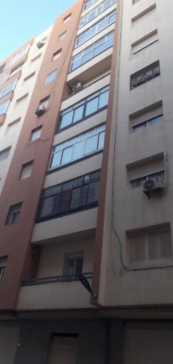 A multi-story building with a beige facade, multiple windows, and balconies. - Mes haws: apartment - Oran, Algeria (Oran)