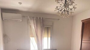 Et soveværelse med en træseng, et natbord, en lampe, et vindue med gardiner og en aircondition.