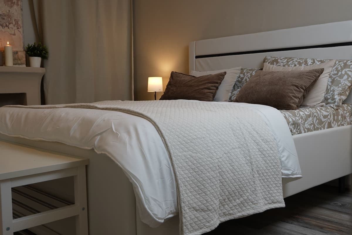 Un dormitorio ordenado con cama, mesita de noche y lámpara.