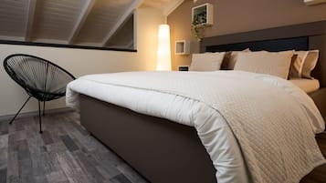 Une chambre à coucher avec un grand lit, un fauteuil moderne et une lucarne.