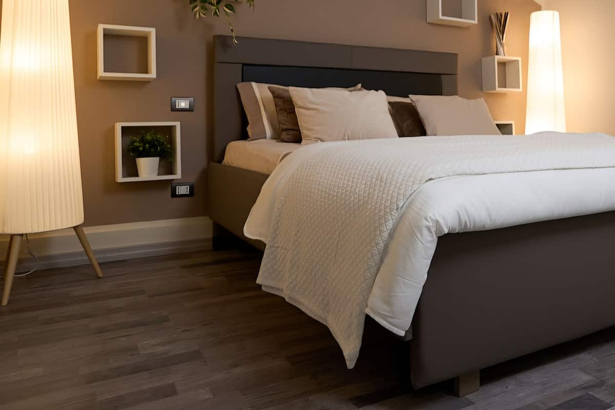 Un dormitorio moderno con una cama grande, mesitas de noche y un estante en la pared con una planta.