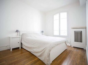A bedroom with a bed, two bedside tables, a window, and a radiator.