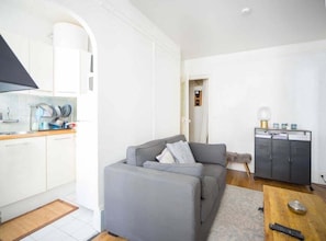 A compact living space with a kitchenette, a grey sofa, a small table, and a cabinet.