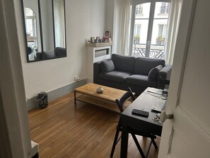A living room with a sofa, a coffee table, a dining table with chairs, a mirror, and a window with a view of buildings.