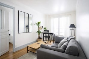 A modern living room with a sofa, a coffee table, a dining table with chairs, a lamp, and a large mirror on the wall.