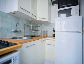 A kitchen with white cabinets, a microwave, a refrigerator, a sink, and a wine bottle.