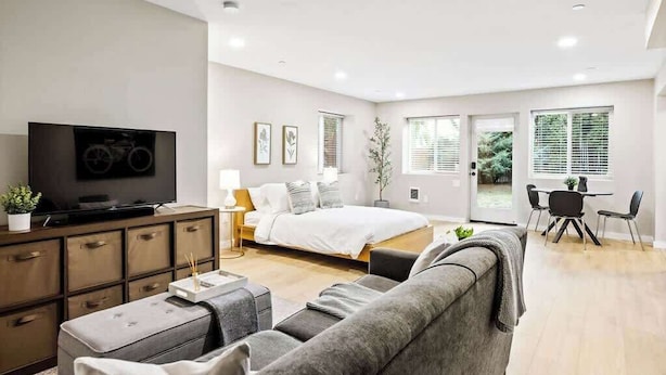 Una sala de estar moderna con televisor de pantalla plana, sofá, comedor y un dormitorio con cama y ventana.