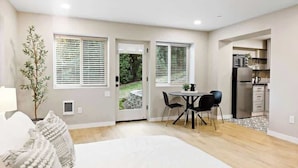 Un dormitorio moderno con una cama grande, una zona de comedor con mesa y sillas, y una cocina visible a través de una puerta abierta.