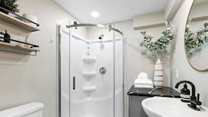 Un baño moderno con ducha de vidrio, lavamanos blanco y espejo.