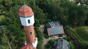 Een toren met een rood dak, omgeven door weelderige begroeiing en een veld met zonnepanelen.