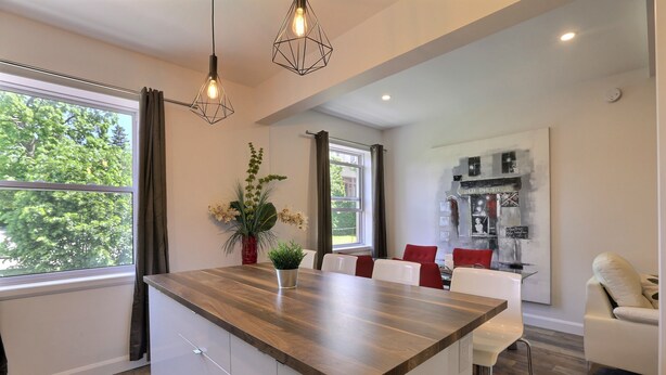 Una cucina moderna con un piano di lavoro in legno, mobili bianchi e un'area pranzo con sedie bianche e cuscini rossi.