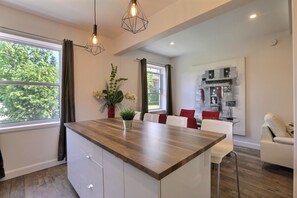 Una cocina moderna con encimera de madera, armarios blancos y un comedor con sillas blancas y cojines rojos.