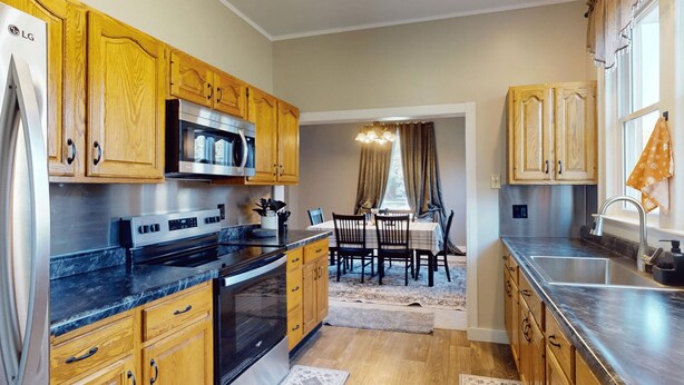 A kitchen with wooden cabinets, a stainless steel refrigerator, and a dining area with a table and chairs.