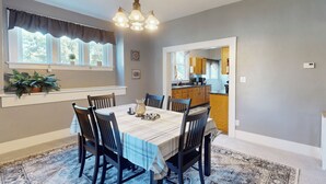A dining area with a table set for six, surrounded by chairs, a chandelier, and a window with curtains.