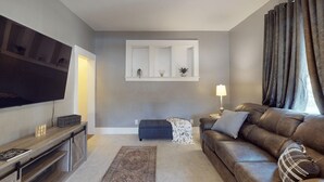A living room with a flat-screen TV, a sofa, a coffee table, and a small side table with a lamp.