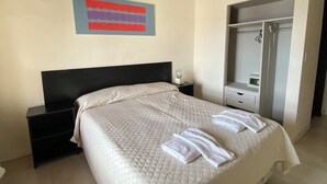 A hotel room with a bed, a nightstand, a bedside table, a mirror, and a wardrobe.