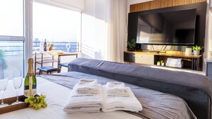 A hotel room with a bed, a TV, a bottle of champagne, and a view of the balcony. - Apt vista incrivel piscina e academia (São Paulo)