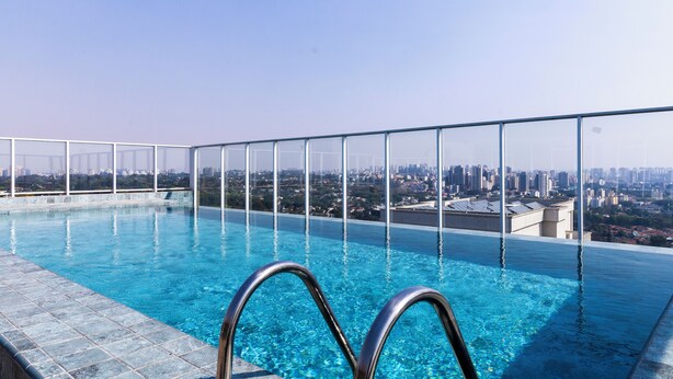 An infinity pool with clear blue water, surrounded by a glass railing, offering a city view. - Apt vista incrivel piscina e academia (São Paulo)