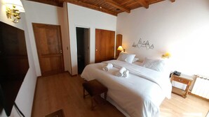 Ein Hotelzimmer mit Holzboden, einem Bett mit weißen Leinentüchern, einem Nachttisch mit Lampe und einer Wand mit Bergmotiv.