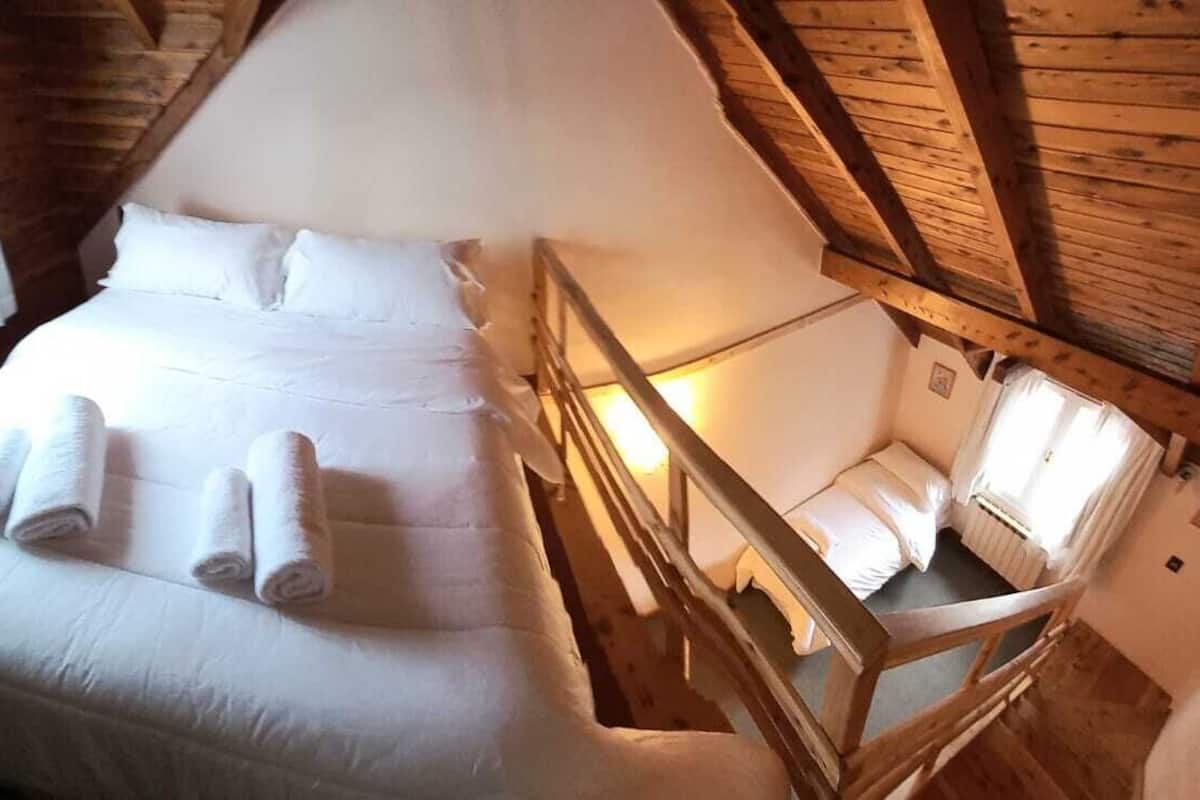A cozy room with a wooden ceiling, a bed with white linens, and a small seating area with a wooden bench.