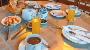 Ein Frühstückstisch reichhaltig gedeckt mit verschiedenen Speisen, darunter Brot, Obst und Getränke.