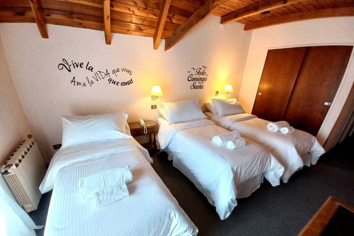 A hotel room with three beds, each with white linens and towels, wooden headboards, and a wooden ceiling.
