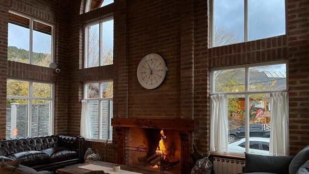 Ein gemütliches Wohnzimmer mit Kamin aus Ziegelsteinen, Ledersofas und großen Fenstern mit Blick ins Freie.