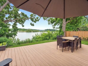 Una terraza de madera con una mesa y sillas, con vista a un lago rodeado de árboles.