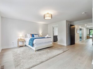 Un dormitorio moderno con una cama grande, una mesita de noche con lámpara y vistas al pasillo.