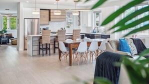Una cocina moderna con una isla central, iluminación colgante y un comedor con mesa y sillas de madera.