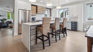 Una cocina moderna con una isla central, sillas de madera oscura, armarios blancos e iluminación colgante.